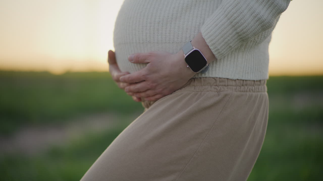 Pregnant Woman Holding Belly at Sunset