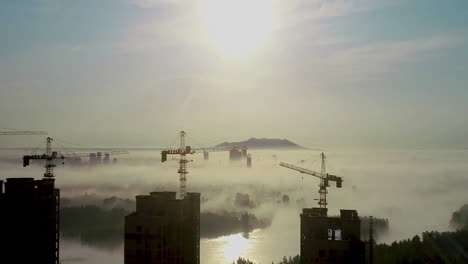 Trabajos-De-Construcción-En-La-Máquina-De-Grúa-Torre-Para-Construir-Una-Torre-Alta,-Edificio-De-Propiedades,-Día-De-Trabajo-Y-Nubes-Que-Fluyen-Sobre-La-Ciudad,-Las-Montañas-Al-Atardecer.