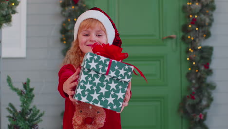 Joyful-toddler-child-girl-kid-in-red-sweater-presenting-one-Christmas-gift-box,-stretches-out-hands