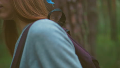 close-up of young hiker pausing in serene forest, hanging bag over shoulder with long hair flowing and blue bandana on, surrounded by tall trees and lush greenery, she holds bag gracefully