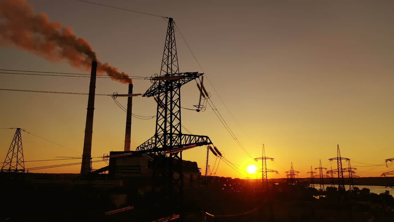 Industrial factory and electricity pylons at sunset. Silhouettes of high voltage power lines against the setting sun. Industrial minimalist landscape.