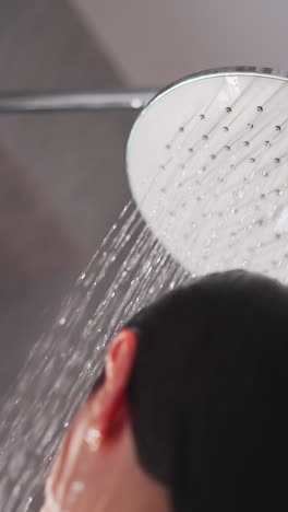 lady takes pleasant shower in apartment. modern big shower head produces streams of water to fall down on naked woman. woman washes in shower with tiled walls