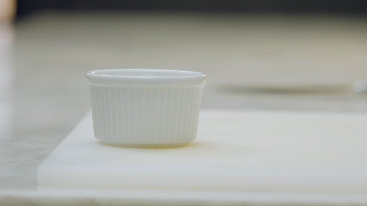 Close-up of a chef placing sugar into an aluminum mold on a cutting board. A white ceramic mold is visible in the blurred background