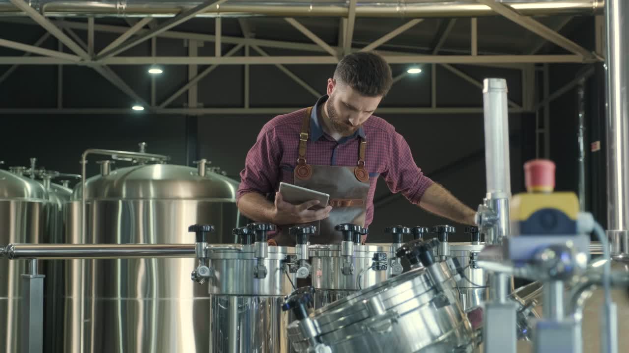 un joven cervecero con un delantal de cuero supervisa el proceso de fermentación de la cerveza en una fábrica de cerveza moderna