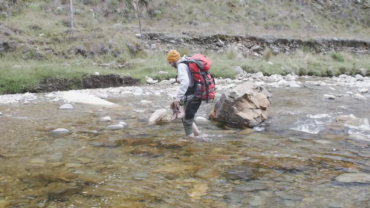 excursionista cruzando el río descalzo mientras sostiene su teléfono