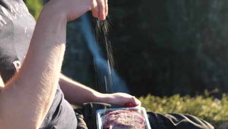 Close-up-shot-of-man-seasoning-meat,-panning-down-revealing-a-juicy-piece-of-rib-eye-entrecôte,-outdoors-in-a-camping-environment