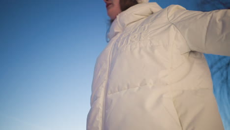 dancer wearing white puffer coat moves body expressively against dark twilight sky captured from low angle showcasing rhythmic posture and flowing coat under soft evening light and snow around