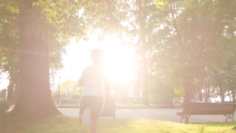 Un-Niño-Con-Una-Camisa-Blanca-Corriendo-En-El-Parque-Hacia-El-Sol,-Tiro-De-Seguimiento