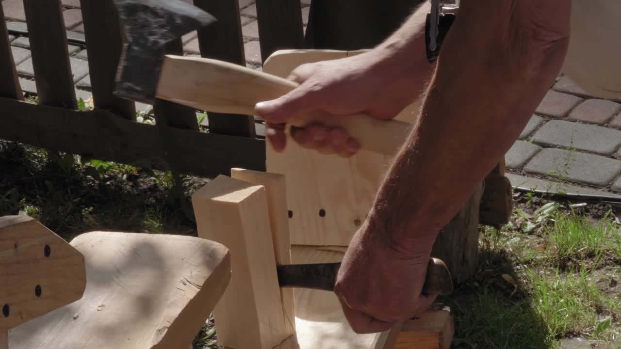 A traditional carpenter tapping an ax splits a small block of wood. He works outside during the event.