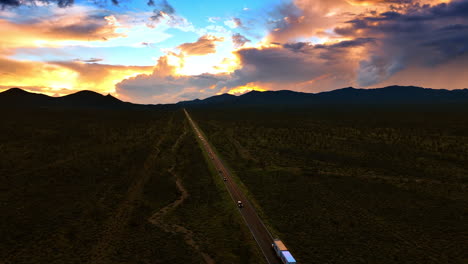 straight highway passing the death valley after sunset. cars with headlights on run by the roads. beautiful colorful sky at backdrop.