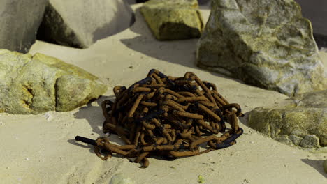 pile of rusty chains resting on sandy ground surrounded by stones