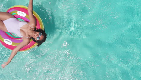 Aerial-of-happy-african-american-teenage-girl-playing-on-inflatable-in-sunny-pool,-copy-space