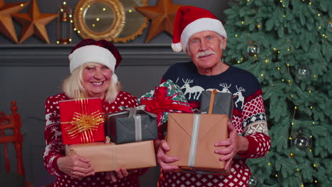 Senior-couple-family-in-Santa-Claus-hats-celebrating-looking-at-camera-holding-Christmas-gift-boxes