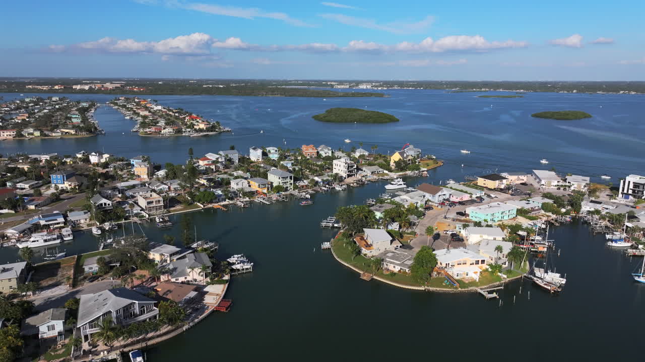 Aerial drone establishing shot of luxury waterfront neighborhood along Boca Ciega Bay near Jack's Boat Basin, featuring colorful homes with private docks on a canal in Saint Pete Beach, Florida