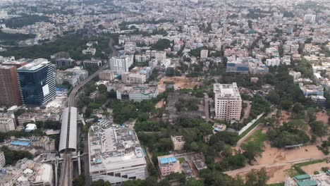 Aerial-cinematic-footage-of-a-city-in-India-shows-buildings-and-trees-paralleling-railroad-tracks-and-a-metro-station-in-the-middle-of-the-city