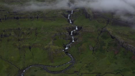 toma aérea ascendente de la cascada klifbrekkufossar que fluye entre enormes acantilados en islandia