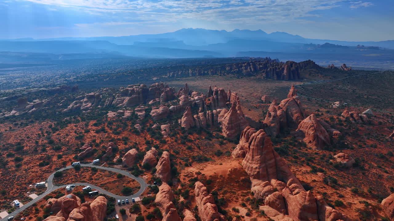 Arches National Park Red Rock Formations and Scenic Views. Arches National Park showcasing iconic red rock spires, winding road, and distant mountains under a partly cloudy sky