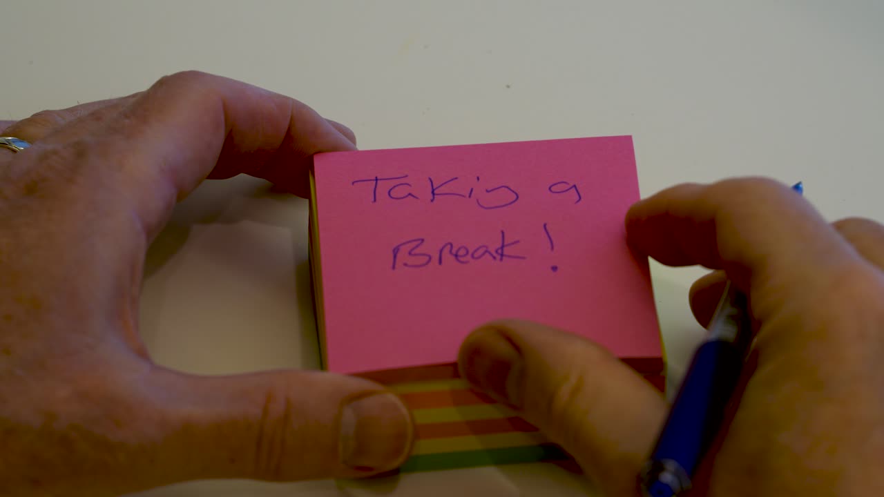 Hand seen writing "Taking a Break" in basic English handwriting on a sticky pad post-it note - isolated close up macro