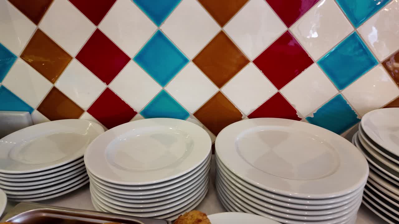 Stacks of Clean White Plates Against Colorful Tiled Wall