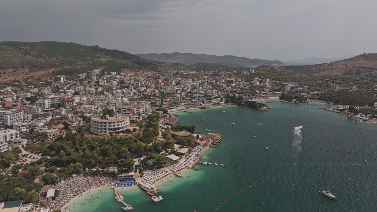Ksamil Arnavutluk Hava Çekimi v9, beyaz kumlu plajı, kıyıdaki tatil kasabasını ve yamaç şehir manzarasını yakalayan turkuaz koy sularının üzerinde uçuyor – Mavic 3 Pro Cine ile çekildi – 18 Temmuz 2024
