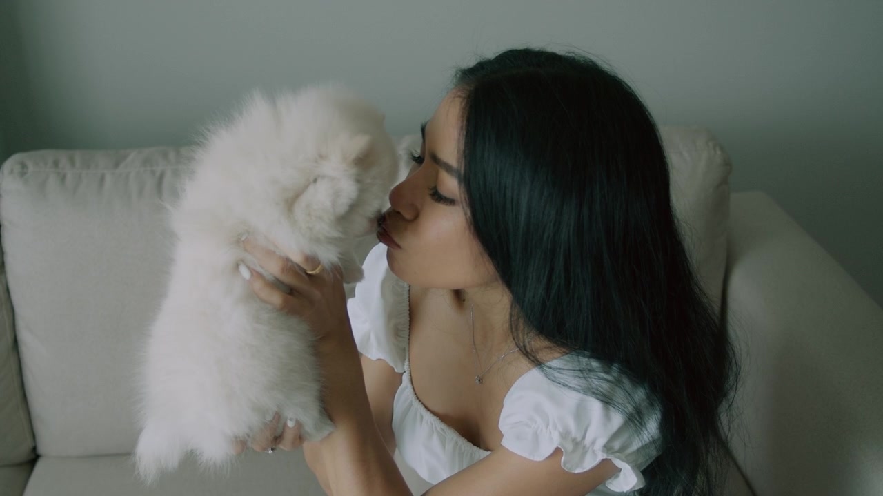Young Woman Cuddling Her Fluffy White Pomeranian Puppy on a Sofa