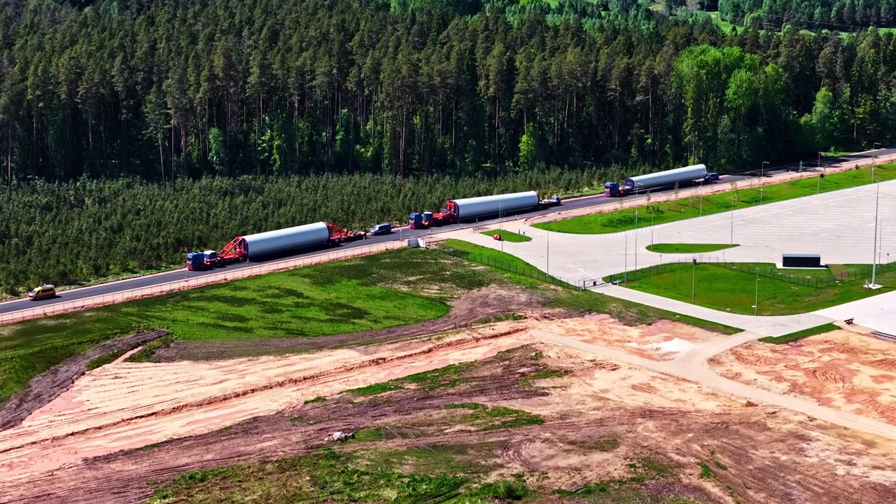 Aerial view of a convoy of trucks transporting large sections of wind turbine towers