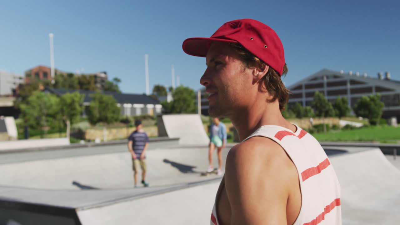 retrato de un hombre caucásico sonriente volviéndose en un día soleado, patinadores en el fondo