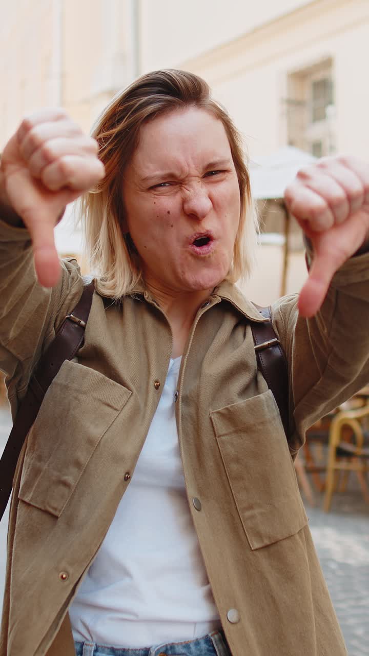 Upset young woman showing thumbs down sign disapproval dissatisfied bad feedback on city street