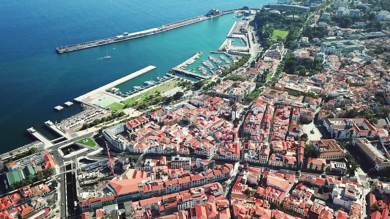 Aerial view of Funchal. Madeira. Portugal, showcasing the cityscape with its red-roofed buildings, a harbor with breakwater and cruise ships with the marina filled with boats, drone shots.