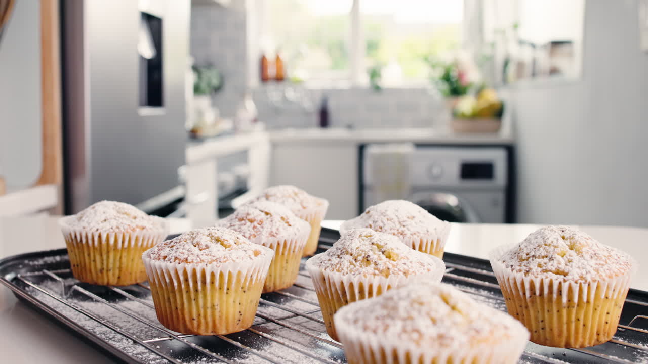 Mano che posiziona muffin appena sfornati con zucchero a velo sul bancone della cucina