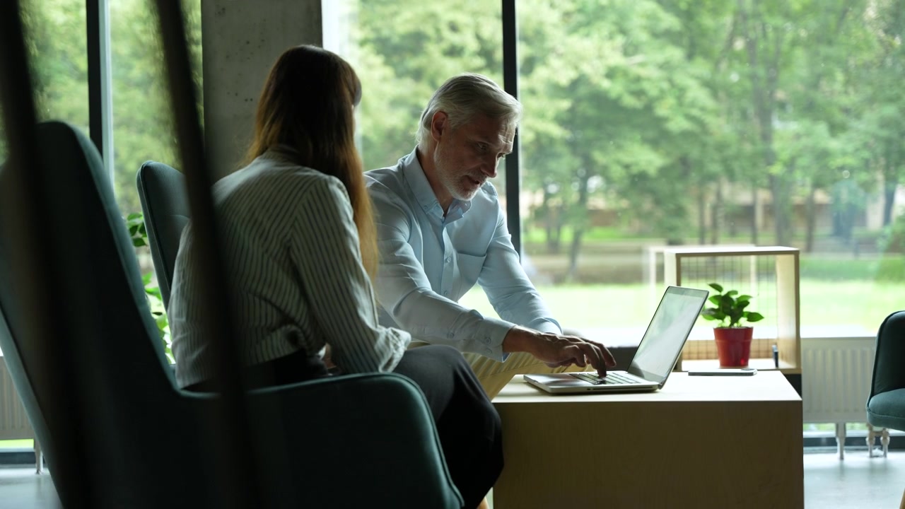 Colleghi professionisti che discutono di lavoro al laptop in una moderna area lounge dell'ufficio.
