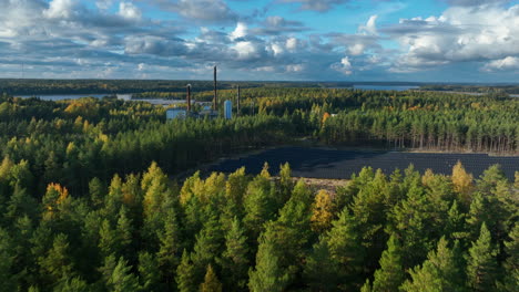 Aerial-view-rising-over-forest,-revealing-a-solar-field,-sunny,-fall-day