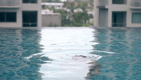 brunette lady swims and dives in pool on roof slow motion