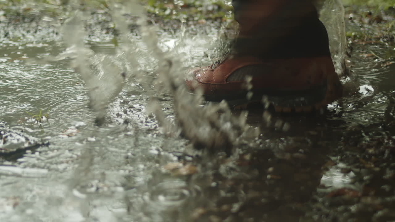 Hiker splashes through puddle in rain, close-up, slow motion