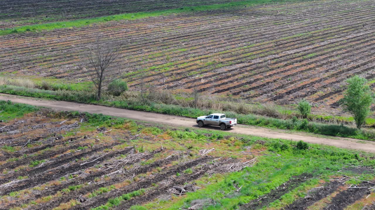 Aerial of deforestation site with truck driving dirt road, cleared land and tree stumps visible below on either side of access point