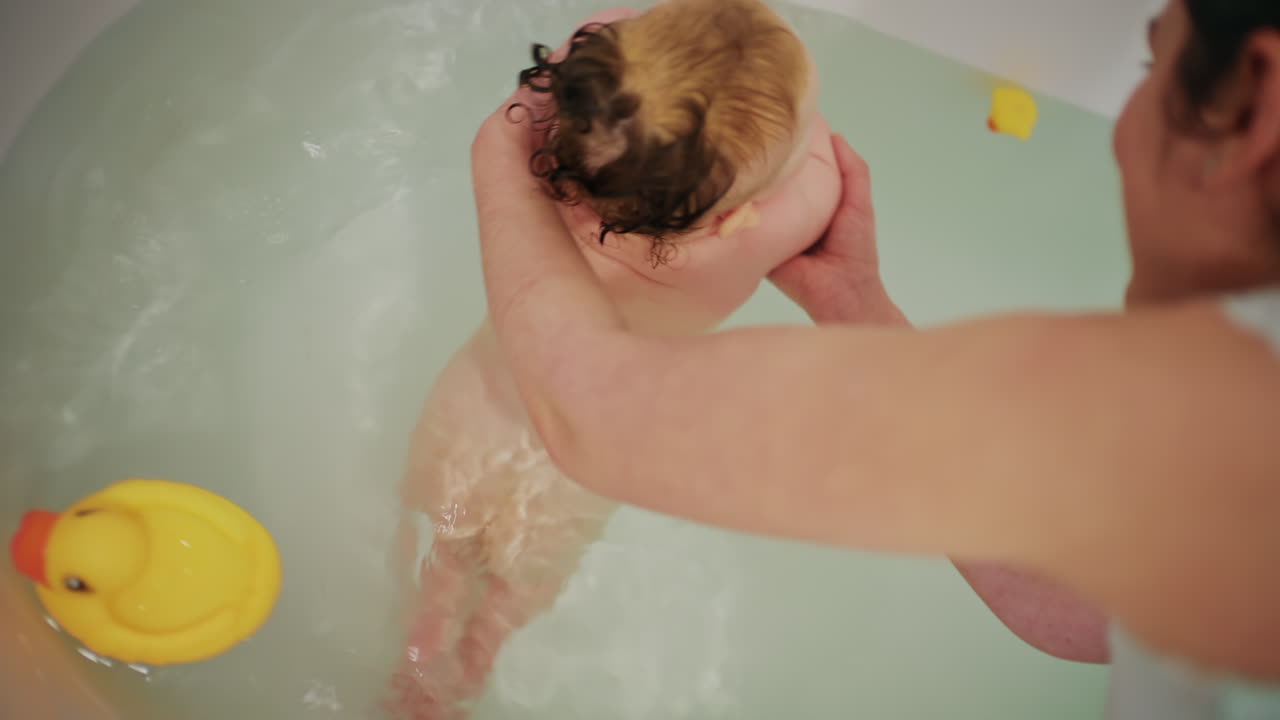Mother holding rubber duck and interacting with baby during bath time