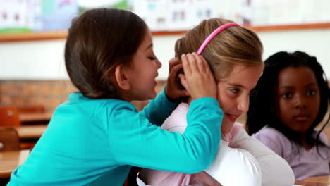 niñas pequeñas contando secretos en el aula.