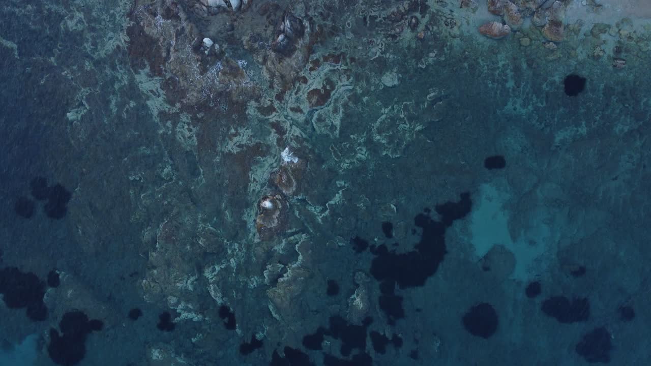 Bird's eye view of a small medieval fortress at the edge of the sea | Beautiful rock formations beneath the shallow sea | Karystos, Greece | 4K