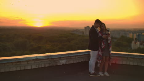 una pareja enamorada está sentada en el techo de la casa. en la distancia las luces de la ciudad nocturna.