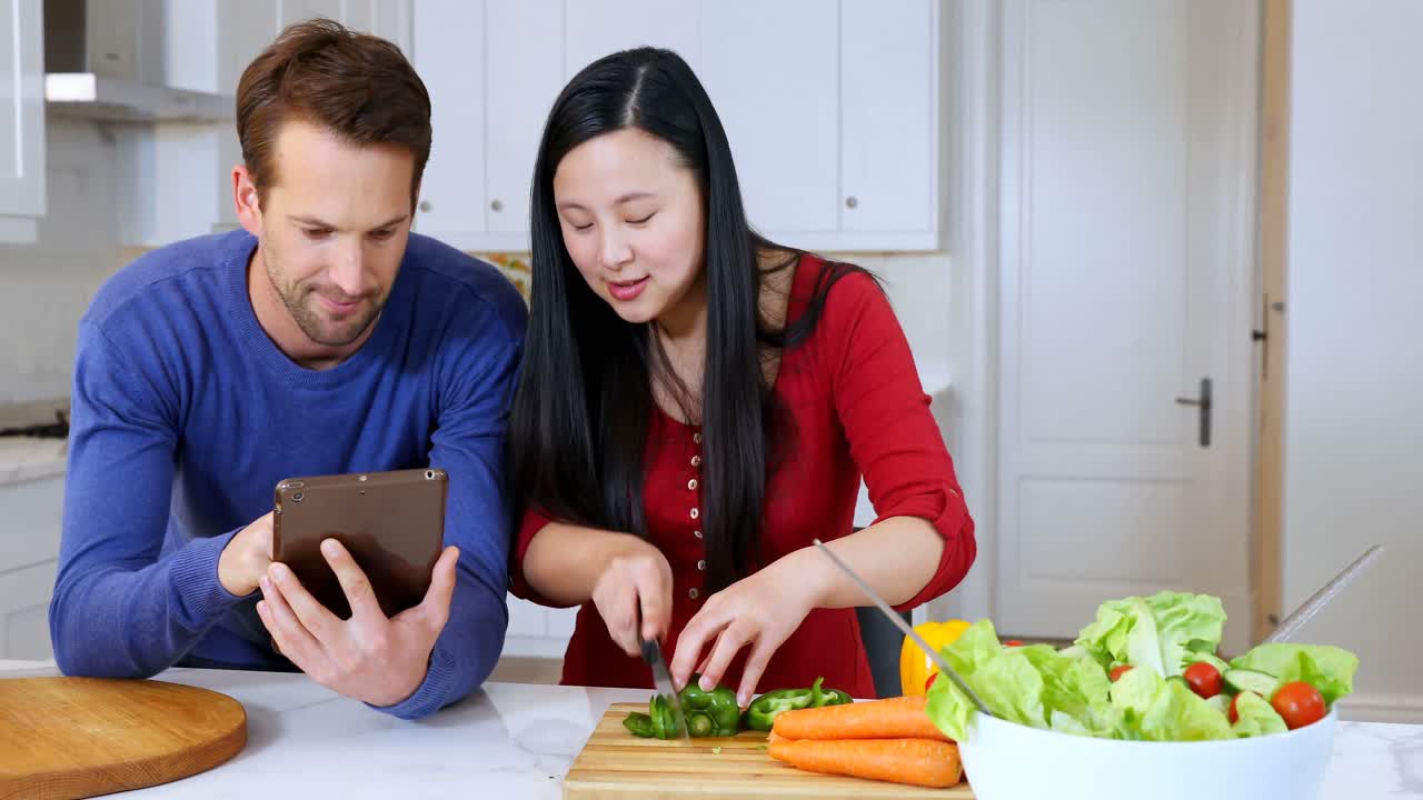 pareja usando una tableta digital mientras corta verduras en la cocina 4k