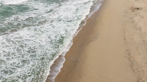 Drone-descends-on-golden-sandy-shores-as-calm-waves-crash-up-along-beach-of-Puerto-Escondido-Oaxaca-Mexico