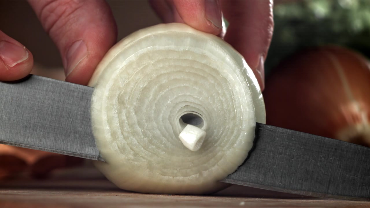 Primo piano di una mano che affetta una cipolla bianca con un coltello