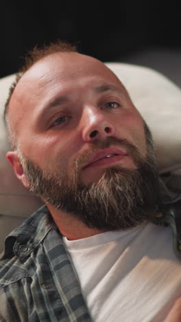 bearded man takes comfortable pose on sofa ready to take capsule. loving wife takes care of husband bringing water and medication at home closeup