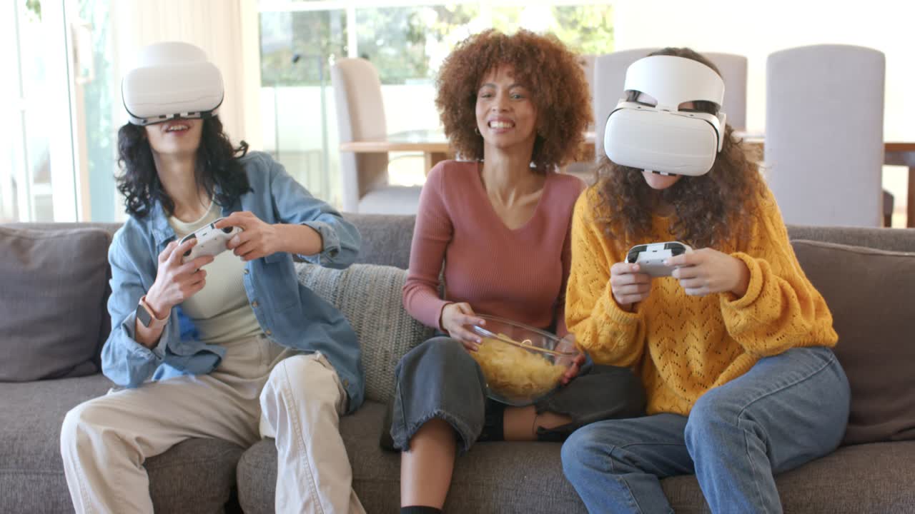 Tre amiche che indossano visori VR, prendono dei controller e si godono degli snack in soggiorno