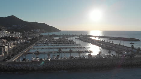 Aerial-drone-ascending-pier-with-port-yachts-,-reveals-blue-horizon-during-sunset