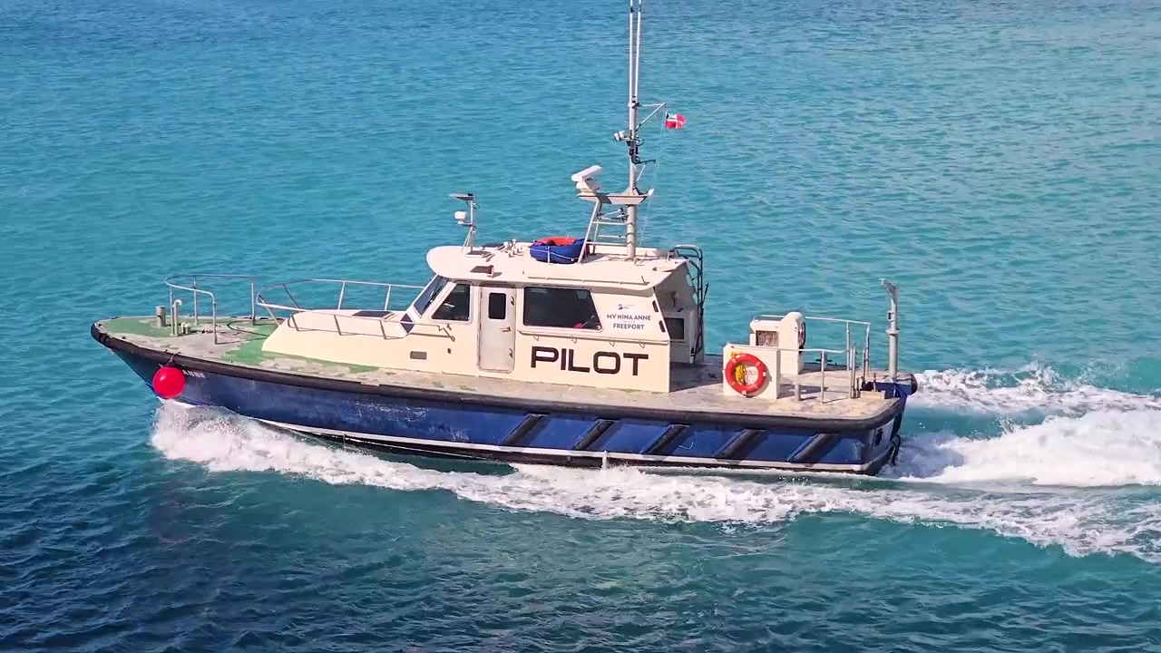 Güneşli bir günde, mavi beyaz bir deniz kılavuz teknesi parlak turkuaz okyanus sularında hızla ilerliyor. Ticari gemi, arkasında beyaz bir iz bırakarak denizde seyrediyor.