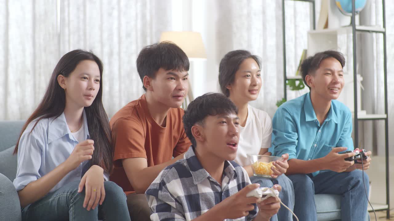 아시아 십대들이 비디오 게임을 하고 집에서 승리를 축하하고 있습니다.