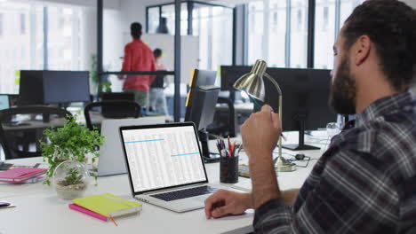 hombre caucásico sentado en el escritorio viendo el procesamiento de datos de codificación en la pantalla del portátil