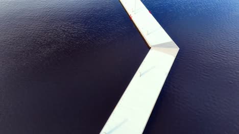 aerial long, wooden pier jutting out into a turquoise ocean