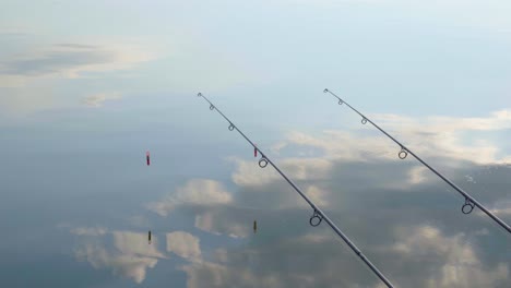 two fishing poles over calm lake reflecting blue sky, clouds, varbo, hungary